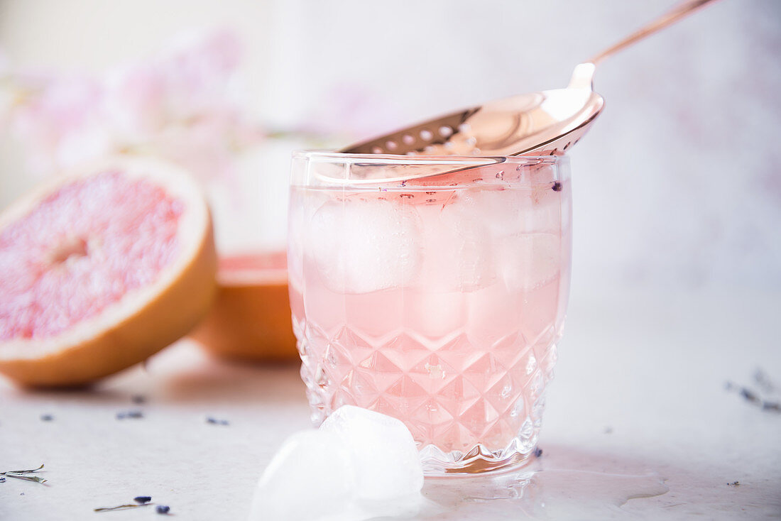 Halved grapefruit, dry lavender, brass strainer, and glasses of grapefruit, gin and lavender fizz with ice cubes