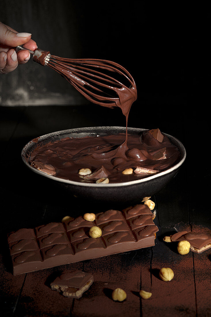 Woman hand with whisk mixing melted chocolate with peanuts in a bowl