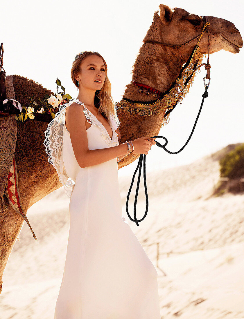 Junge Frau in langem, weißem Brautkleid mit Kamel