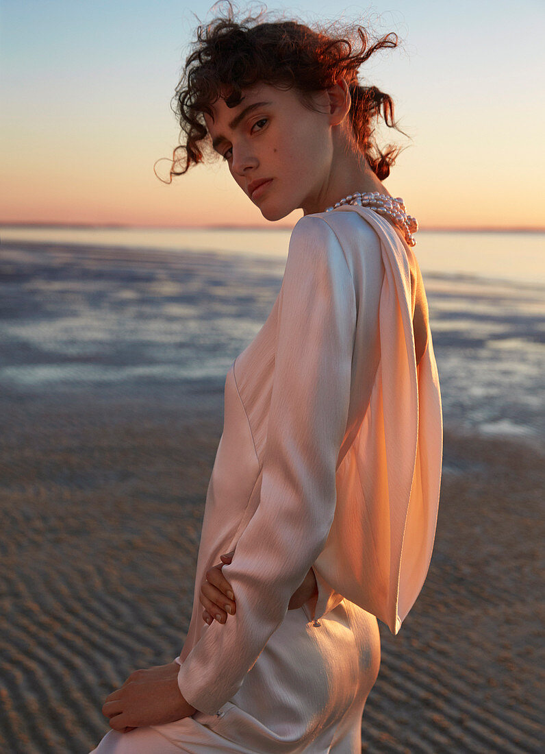 Dunkelhaarige Frau in elegantem Kleid bei Sonnenuntergang am Meer