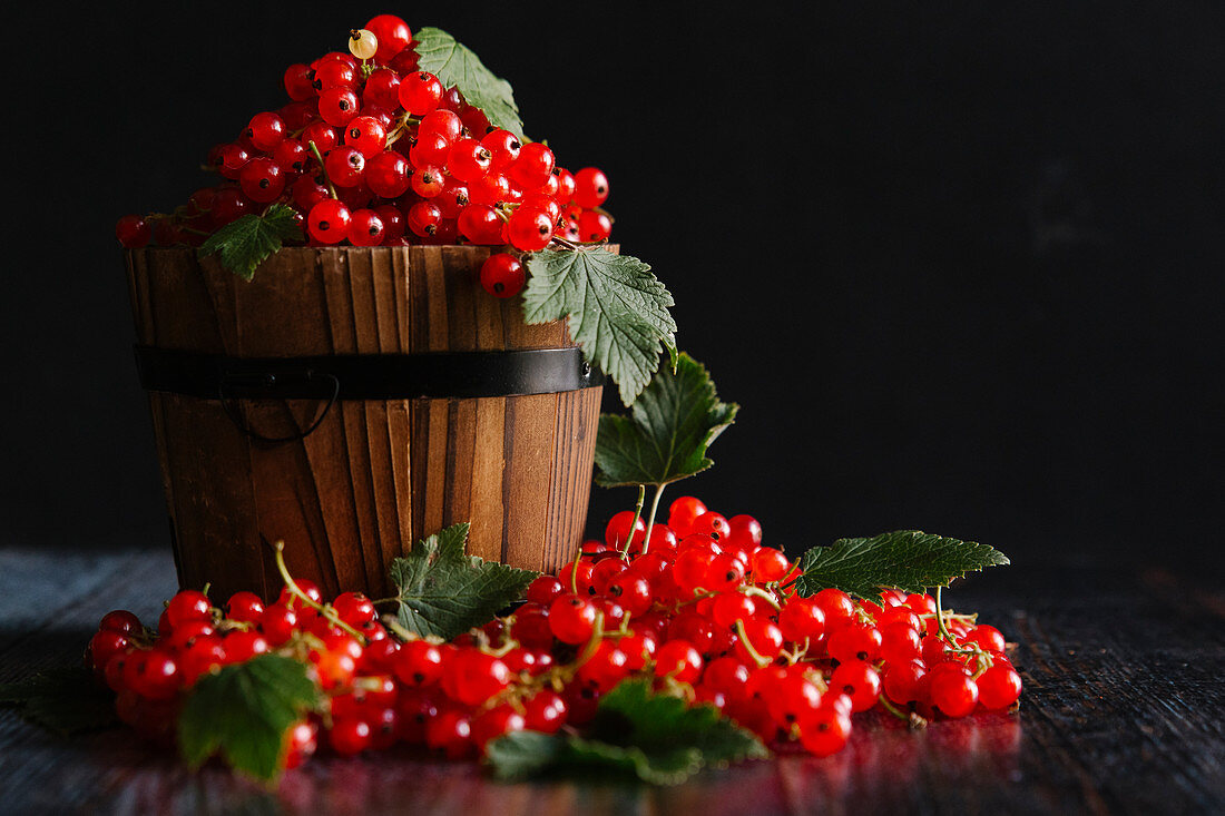 Redcurrants with leaves in and around a wooden basket