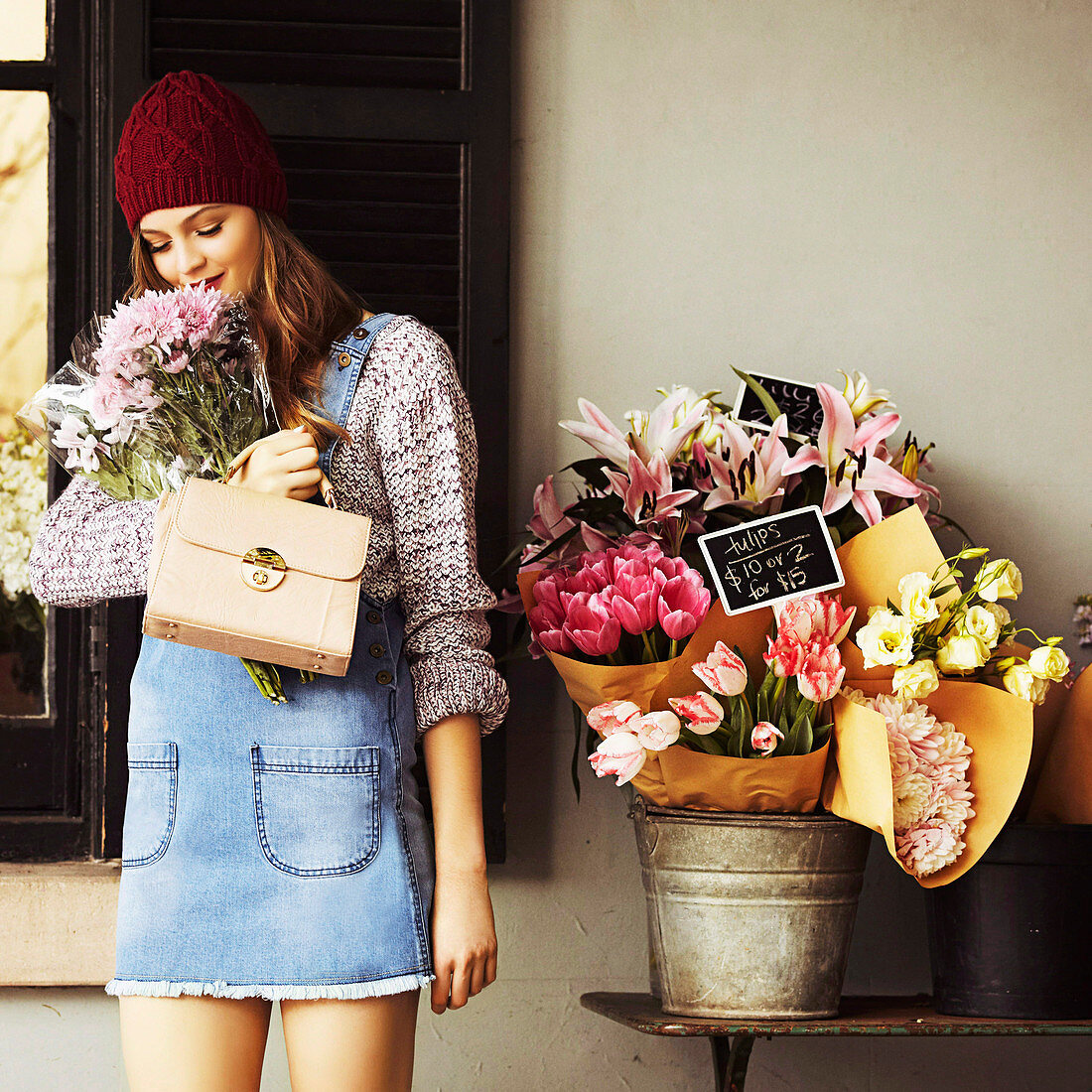 Junge Frau mit Strickmütze im Pulli und Latzkleid vor Blumenladen