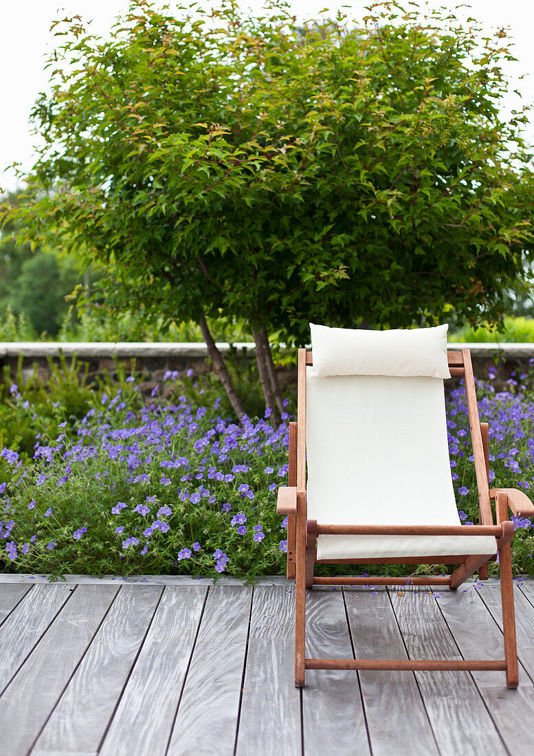 Deck chair on terrace in front of bed of cranesbill geraniums and small tree