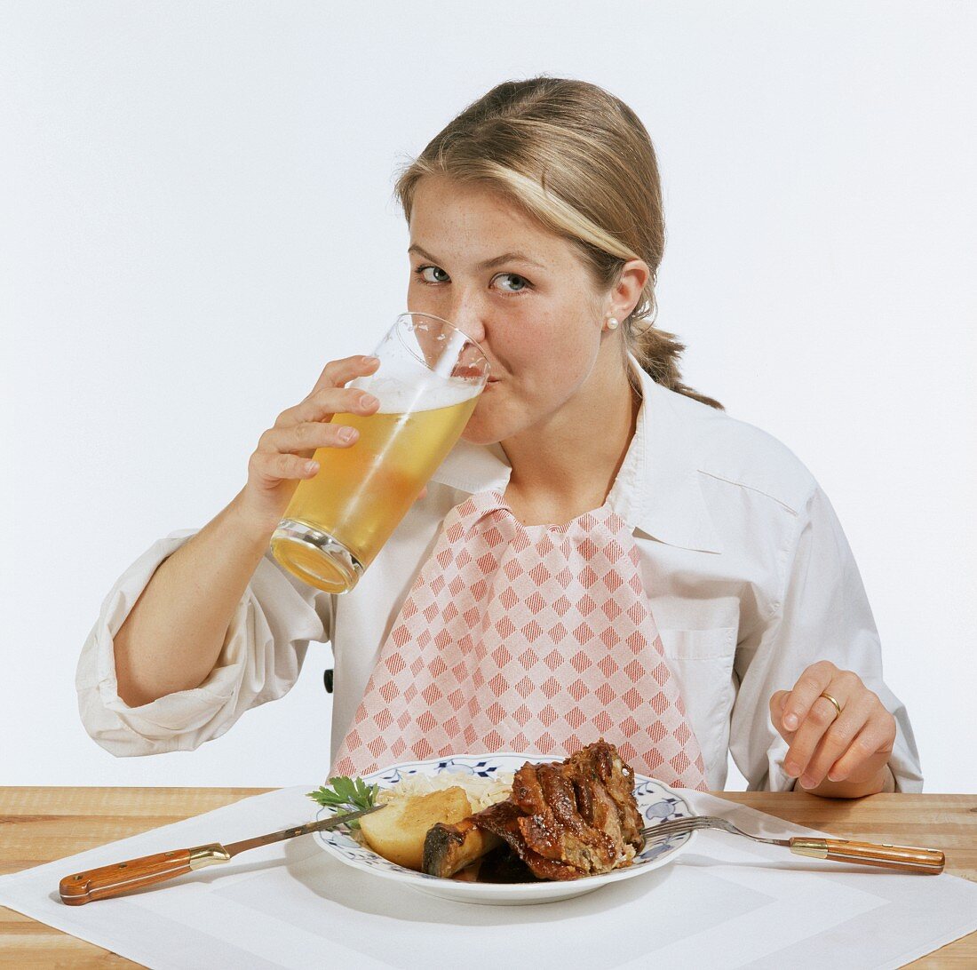 Modell vor Teller mit Schweinshaxe trinkt ein Glas Bier