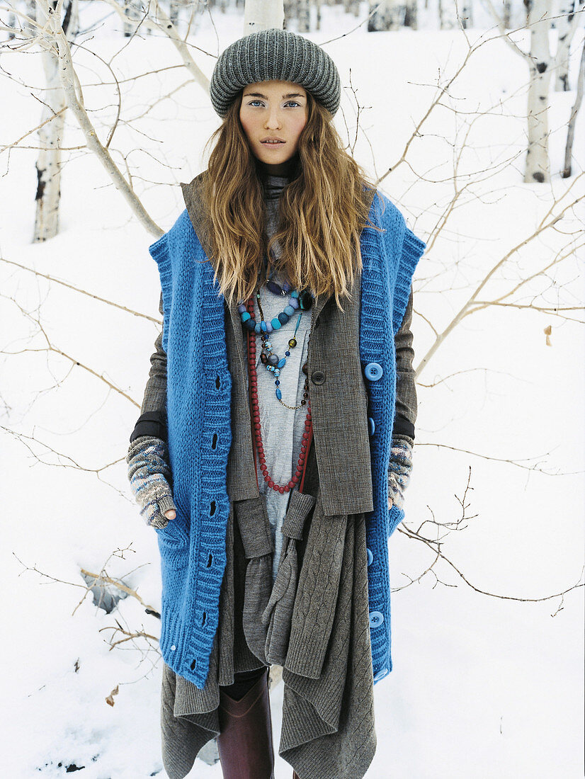 Junge Frau mit Strickmütze in grauer Jacke und blauer Strickweste im Schnee