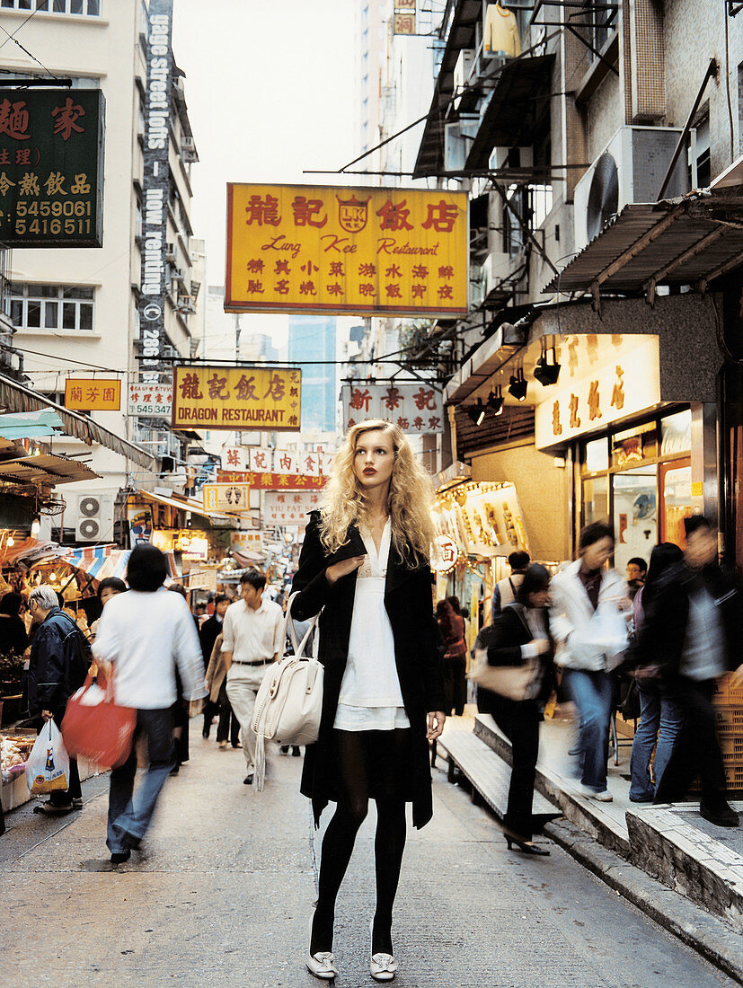 A blonde woman wearing a black-and-white dress and a black coat in a street in Hong Kong