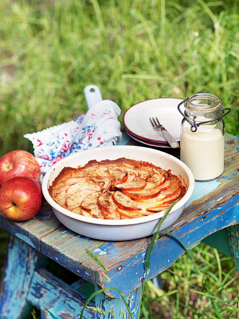 Apple pie in a baking tin, with a glass jar of cream next to it