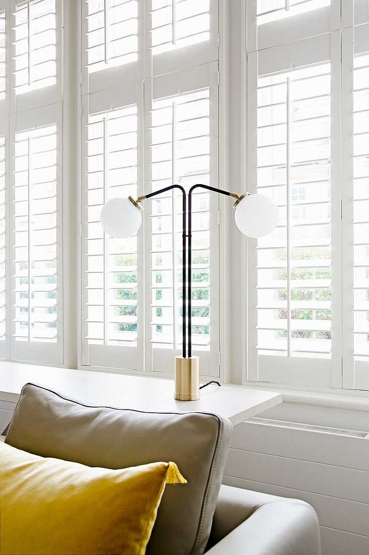 Two-armed table lamp on windowsill behind sofa