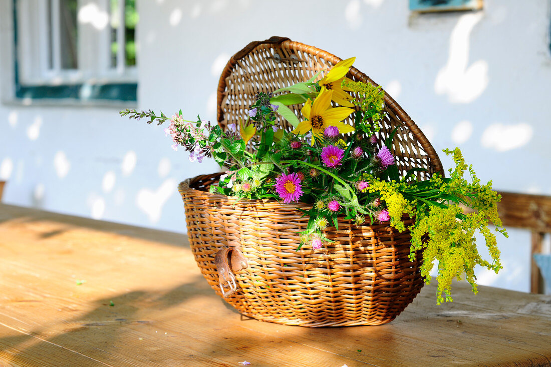 A basket of flowers on a wooden table in front of a house