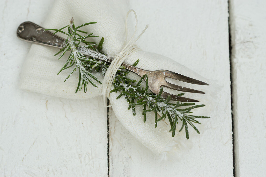 A napkin with a silver fork and a sprig of rosemary