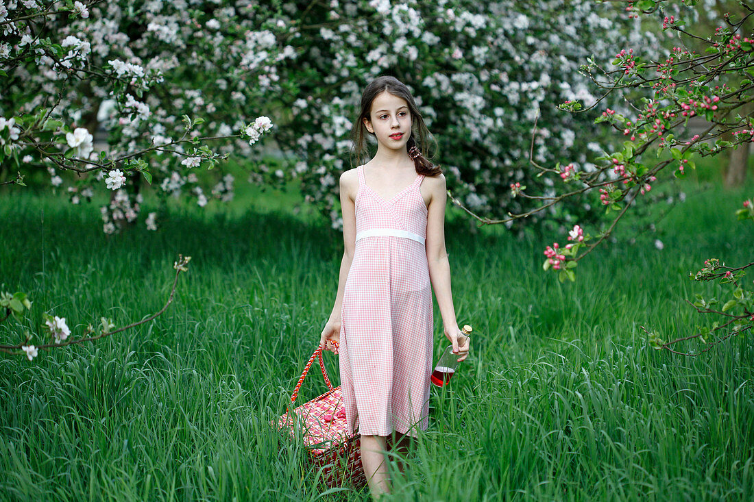 A girl running with a picnic basket in a meadow amongst apple trees