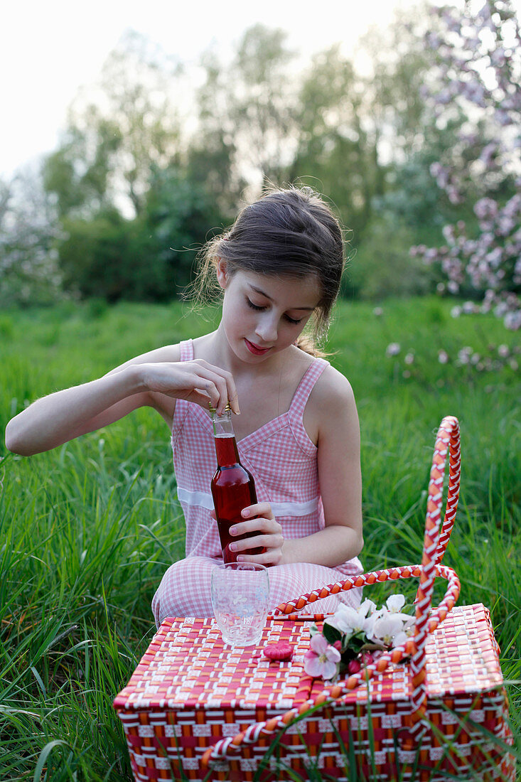 A girl with a juice bottle and basket having picnic in a meadow amongst apple trees