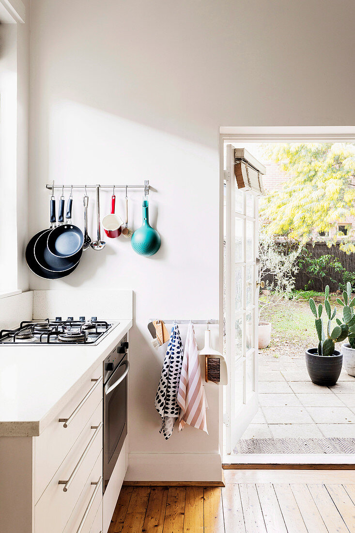 Wall bracket with pans next to open patio door in white kitchen