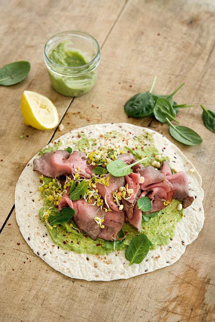 A burrito with roast beef, avocado cream and baby spinach