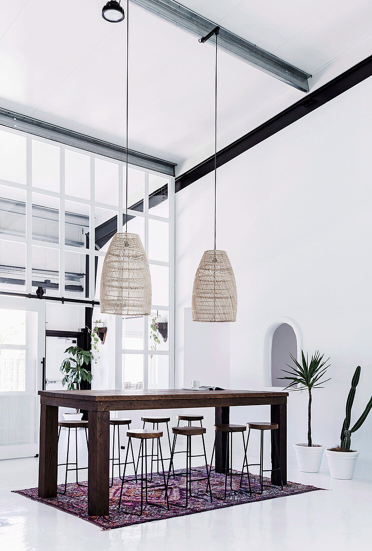 Wooden table with bar stools, above it pendant lights in a high, white room