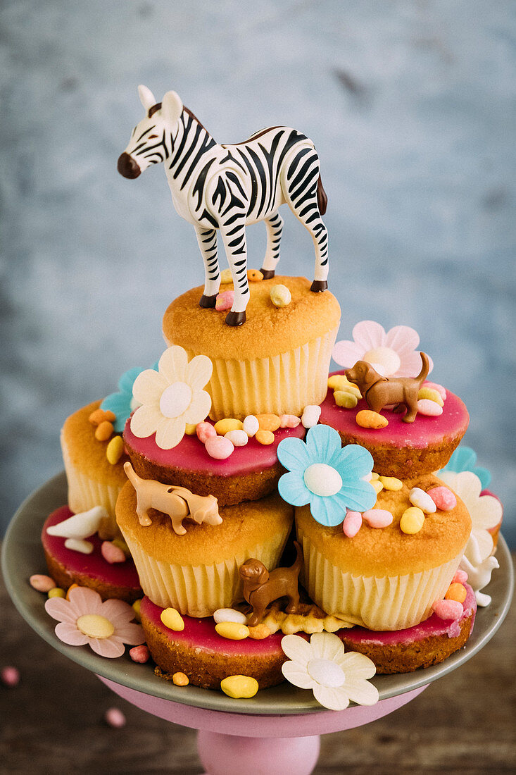 Cupcakes auf Gebäckteller dekoriert mit Tierfiguren, Blüten und Süssigkeiten