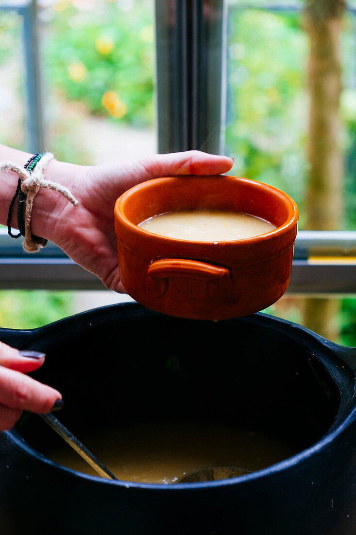 A person filling a bowl with soup from a pot