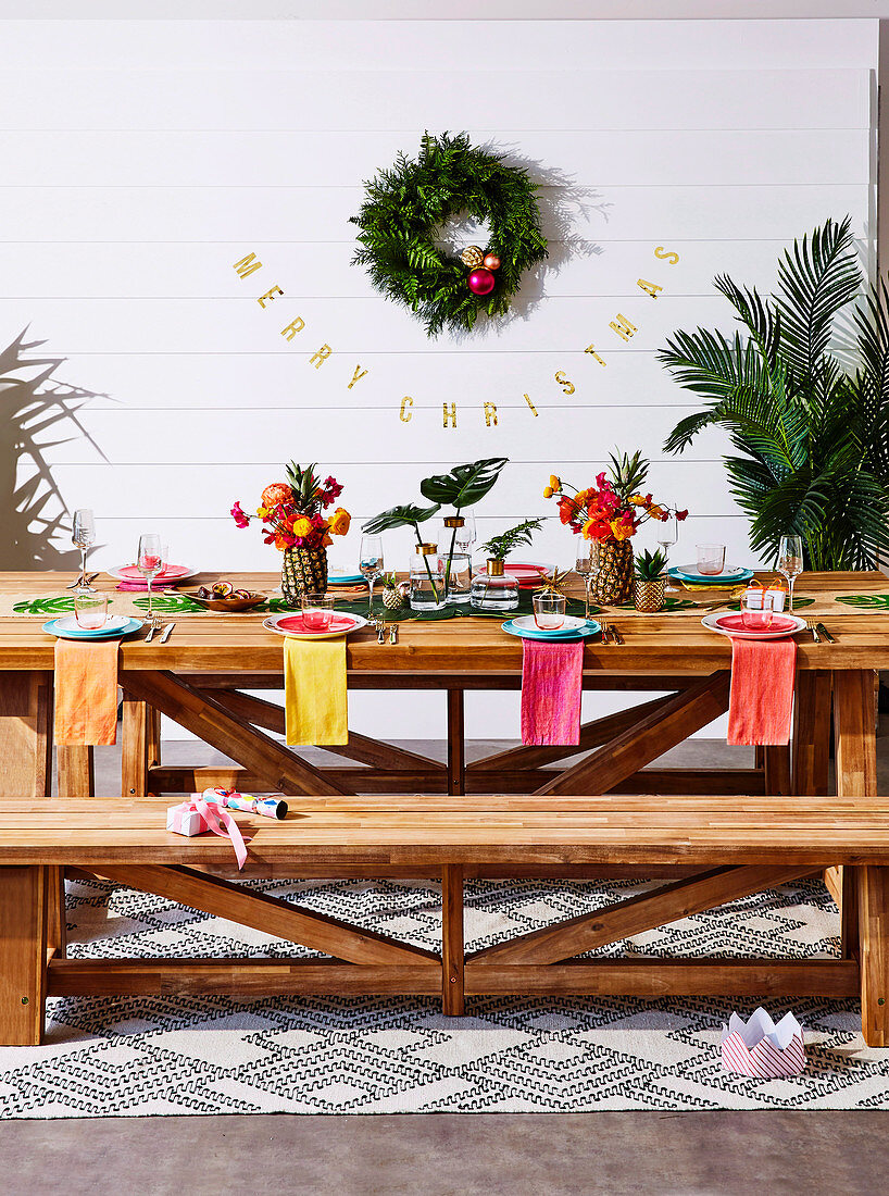 Bunt gedeckter Holztisch mit Bank vor Wand mit Weihnachtsdekoration