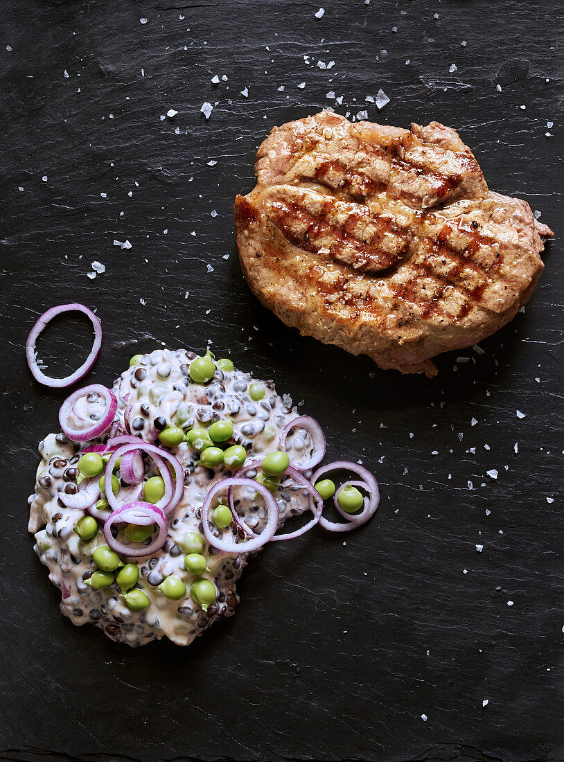 Grilled pork collar steaks with beluga lentils and peas in a yoghurt sauce with red onions