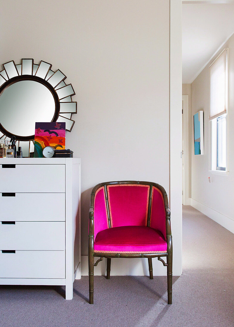 Armlehnstuhl in Pink neben weißer Kommode mit Spiegel
