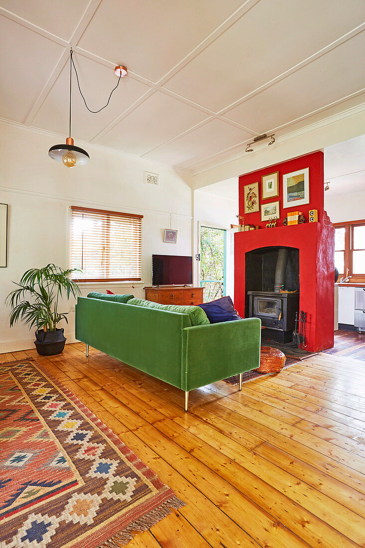 Green sofa and fireplace with red wall covering in the living room with wooden floorboards