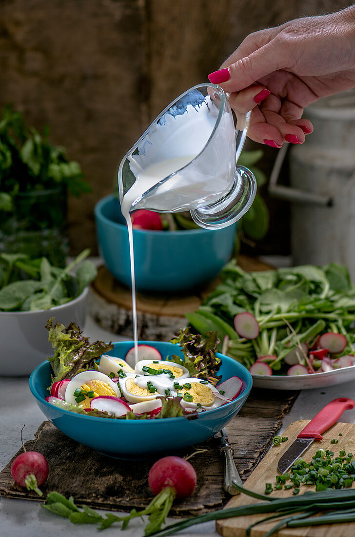 Dressing being poured over a salad with radishes and boiled eggs