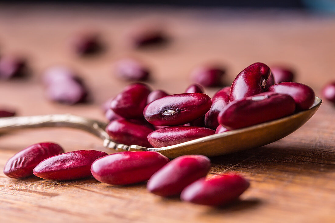 Rote Bohnen auf Löffel und Holzuntergrund (Nahaufnahme)