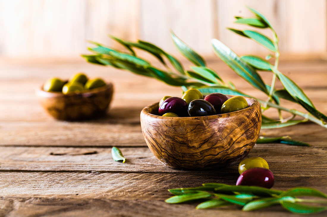 An arrangement of olive sprigs and various olives in a wooden bowl