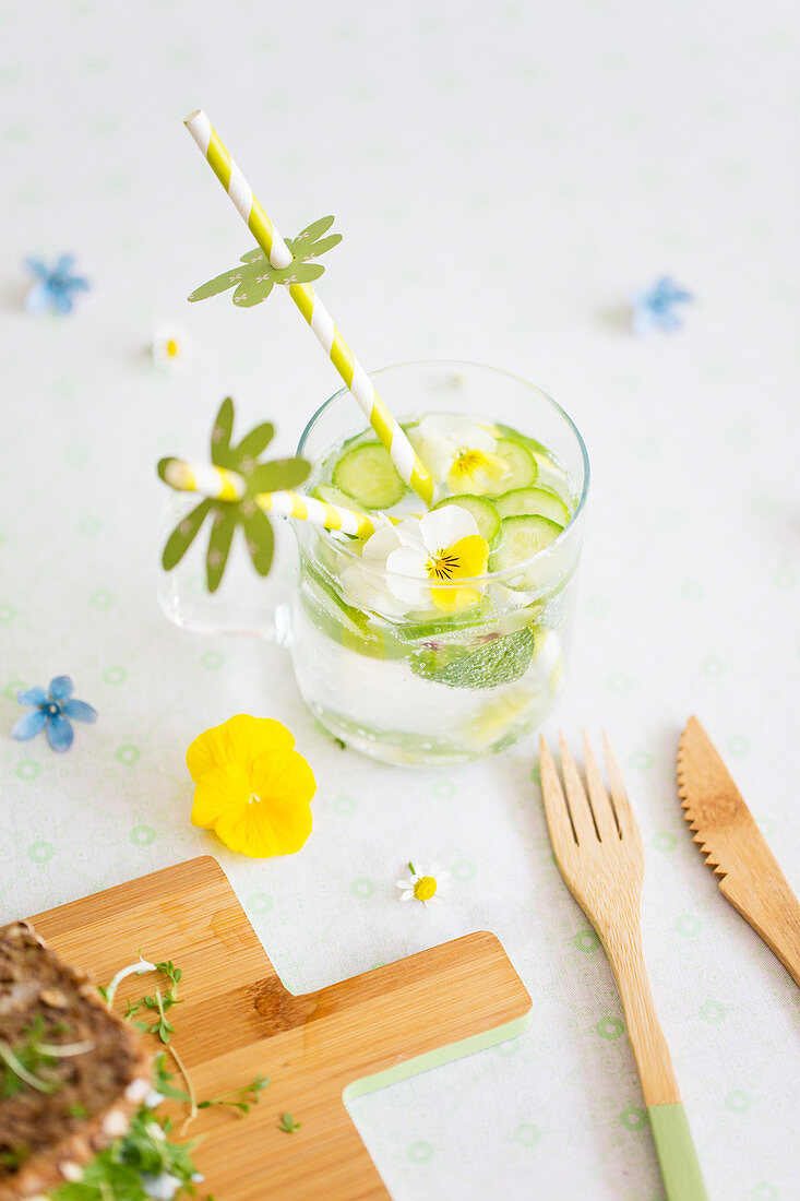 Water with cucumber, edible violas and drinking straws with paper decorations