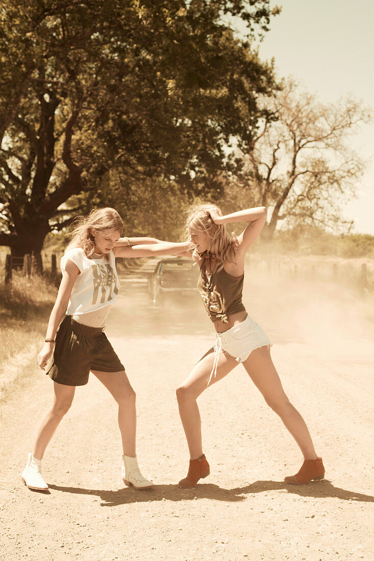 Two women testing their strength on a dusty country road