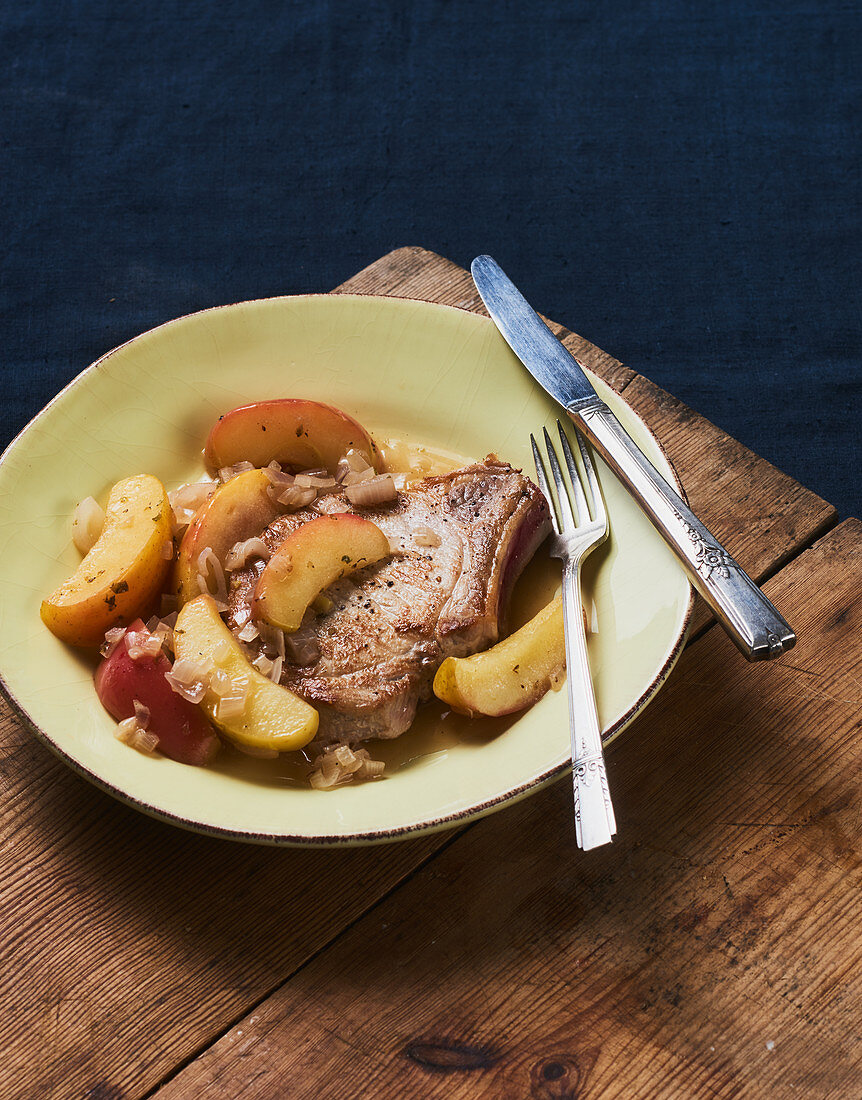 Sauteed Pork Chop with Apples and Herbs on a White Plate