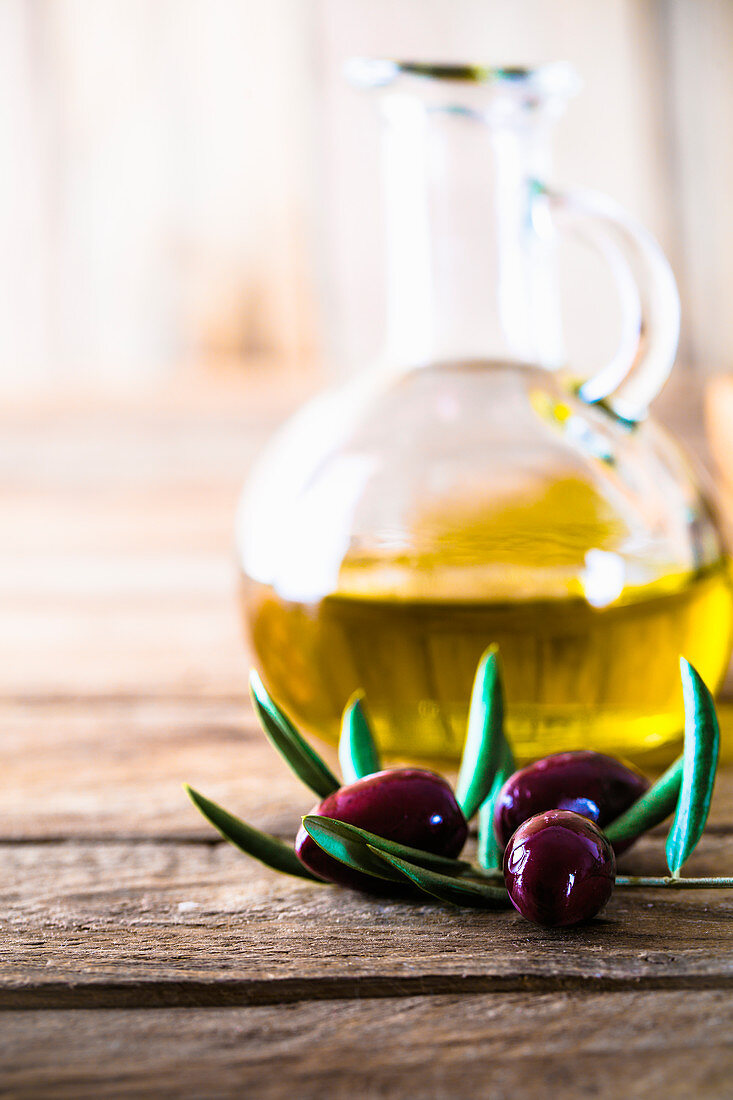 Olive oil in a glass carafe with olives and olive sprigs in front of it