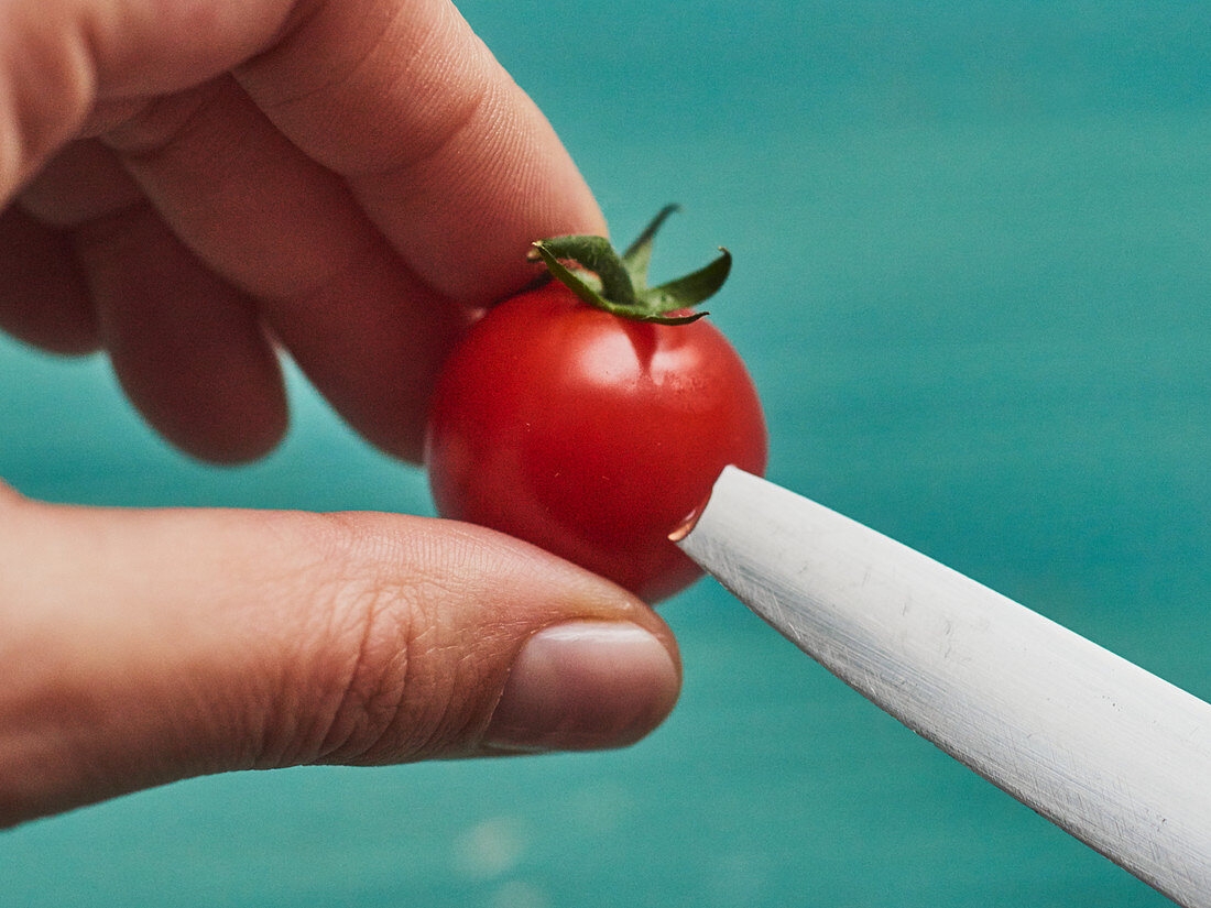 A cherry tomato being pierced with a knife