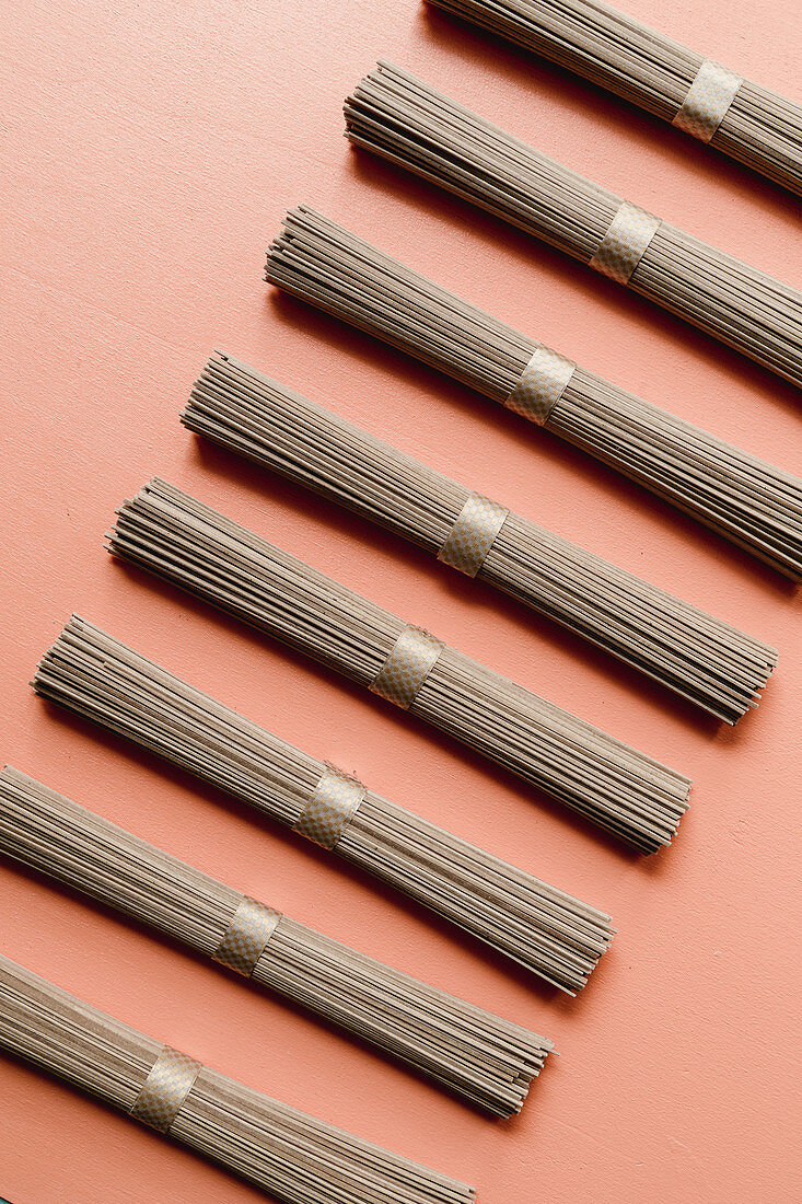 Bundles of soba noodles in a row on a coloured surface