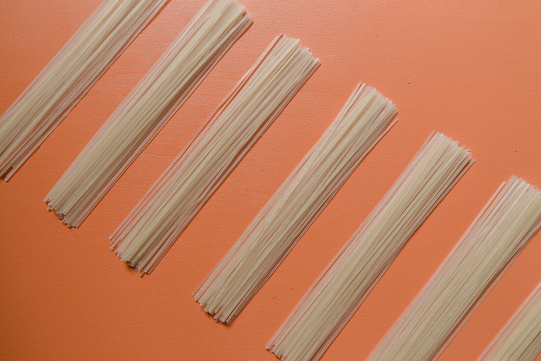 Bundles of rice noodles in a row on a coloured surface
