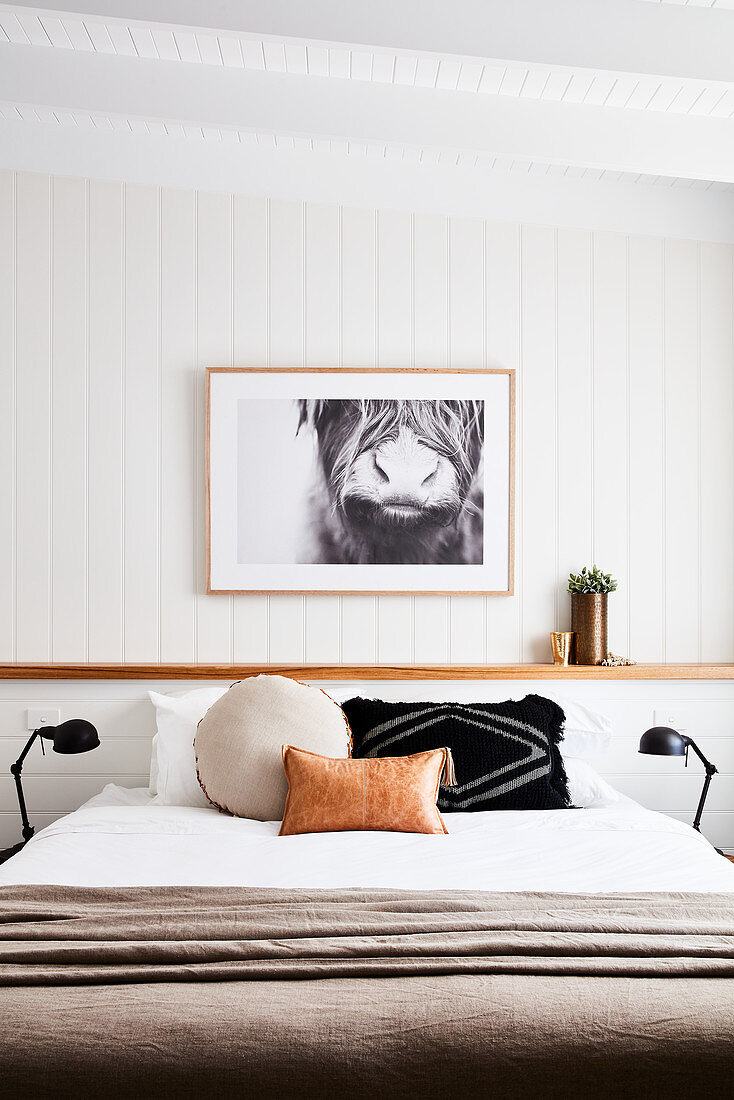 Scatter cushions on double bed in bedroom with white wood-panelled walls