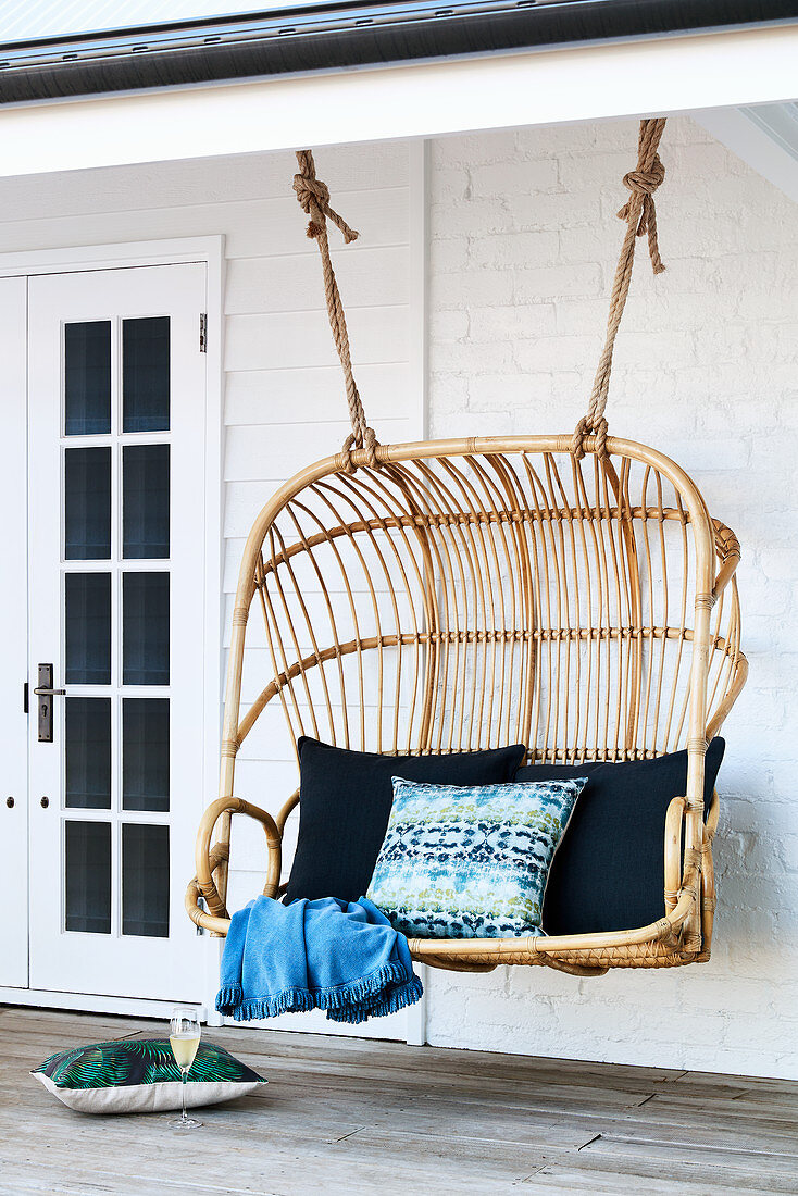 Rattan hanging seat with scatter cushions on veranda