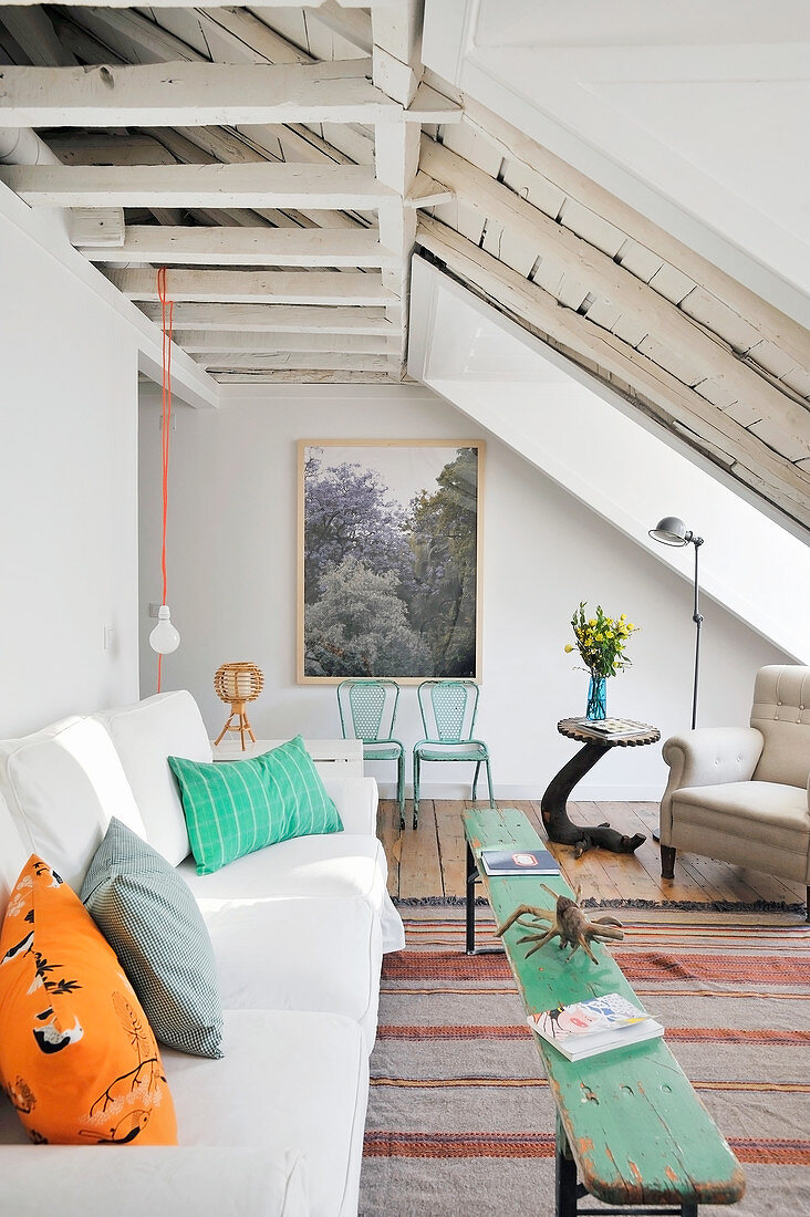 Colourful cushions on white sofa and rustic wooden bench used as coffee table in living room