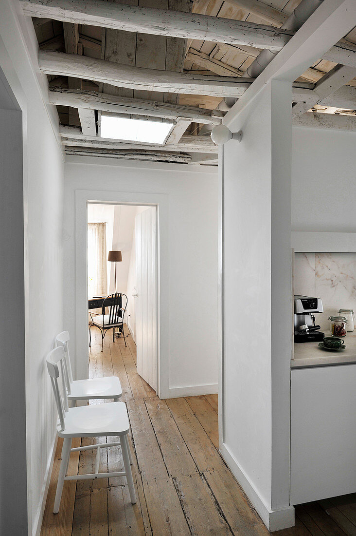 Chairs on rustic wooden floor and kitchen in open-plan interior