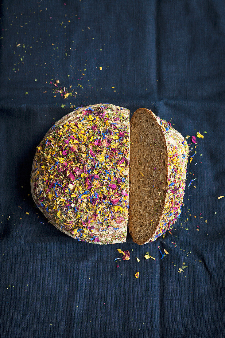 A loaf of wholemeal bread topped with edible flowers, sliced