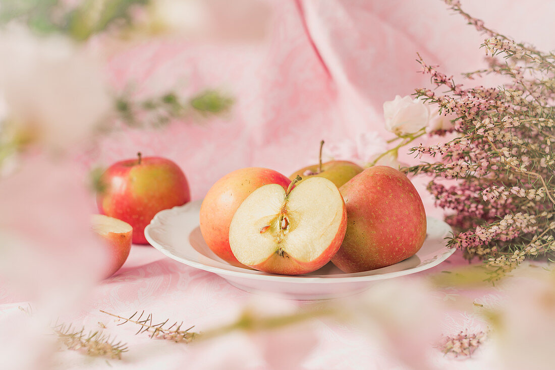 Pink Lady Äpfel auf einem Teller und rosa Blüten vor pastellfarbenem Hintergrund