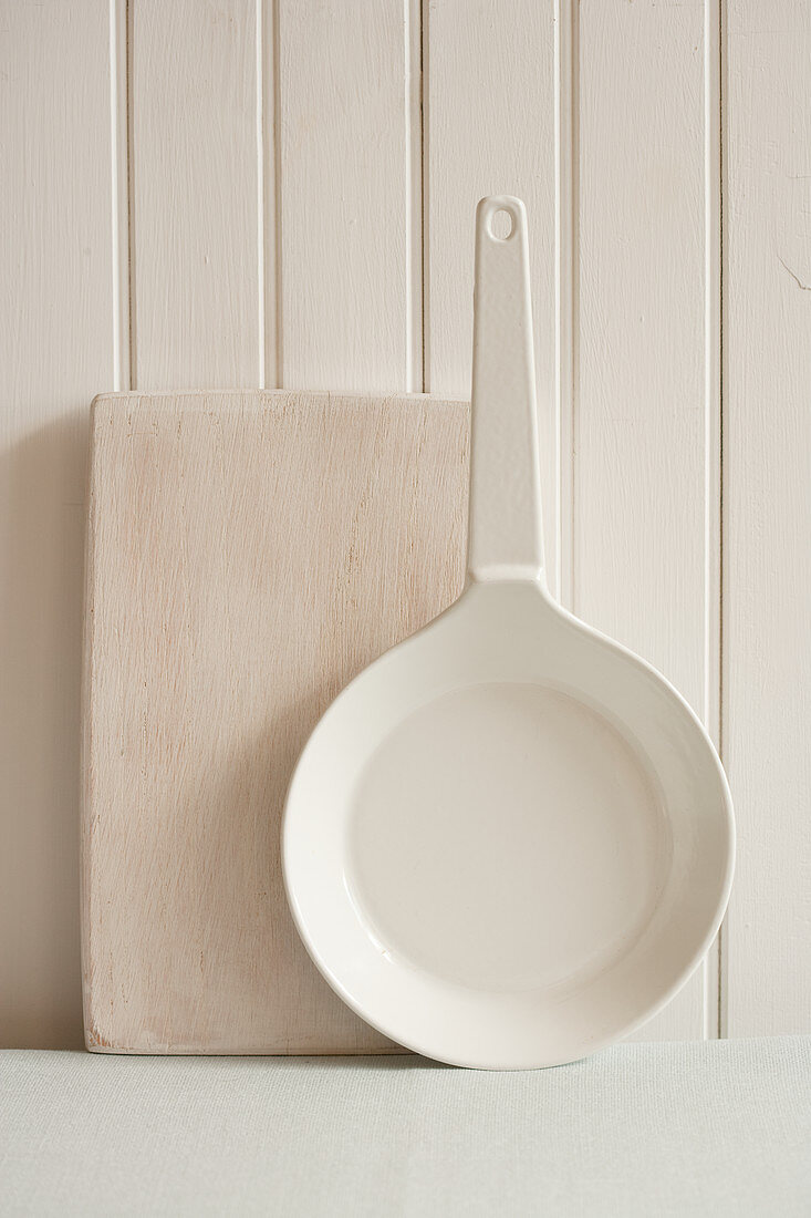 A wooden chopping board and a pan leaning against a light wooden wall