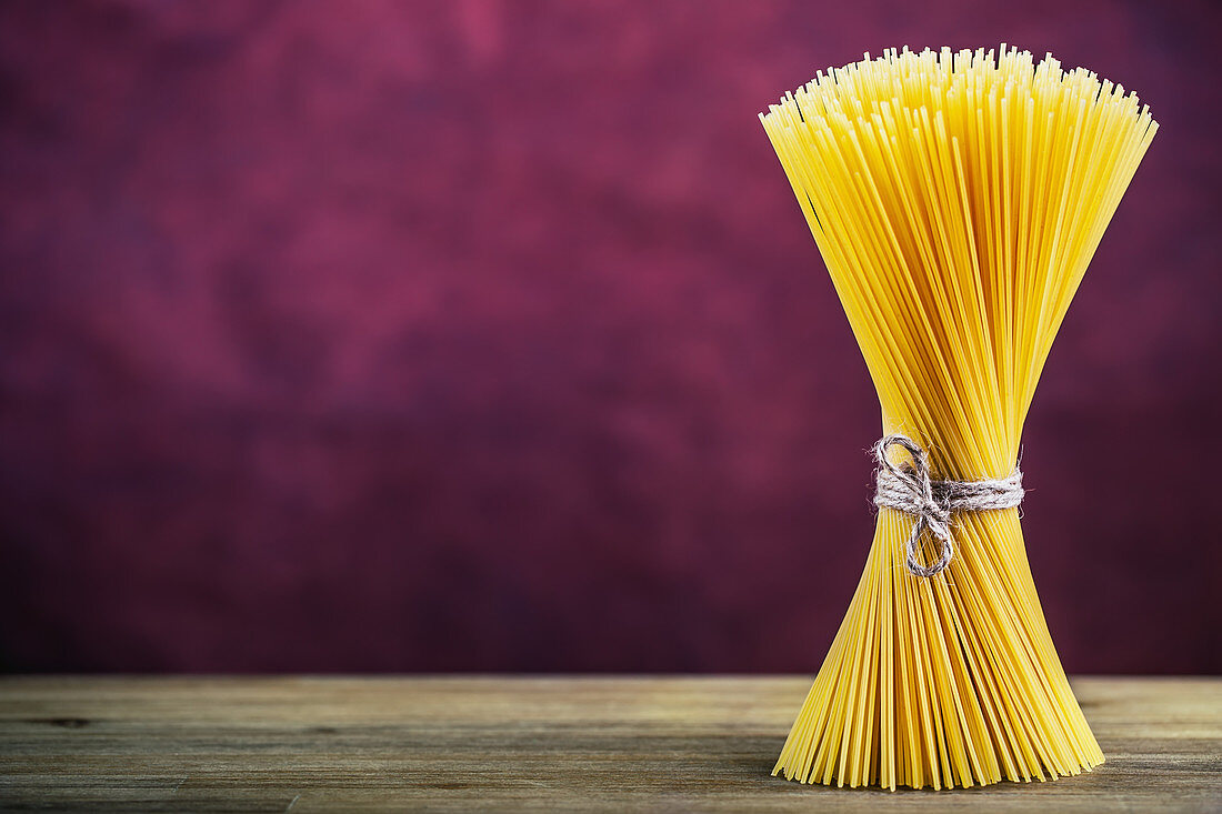 Ein Bund Spaghetti auf Holztisch, vor violettem Hintergrund