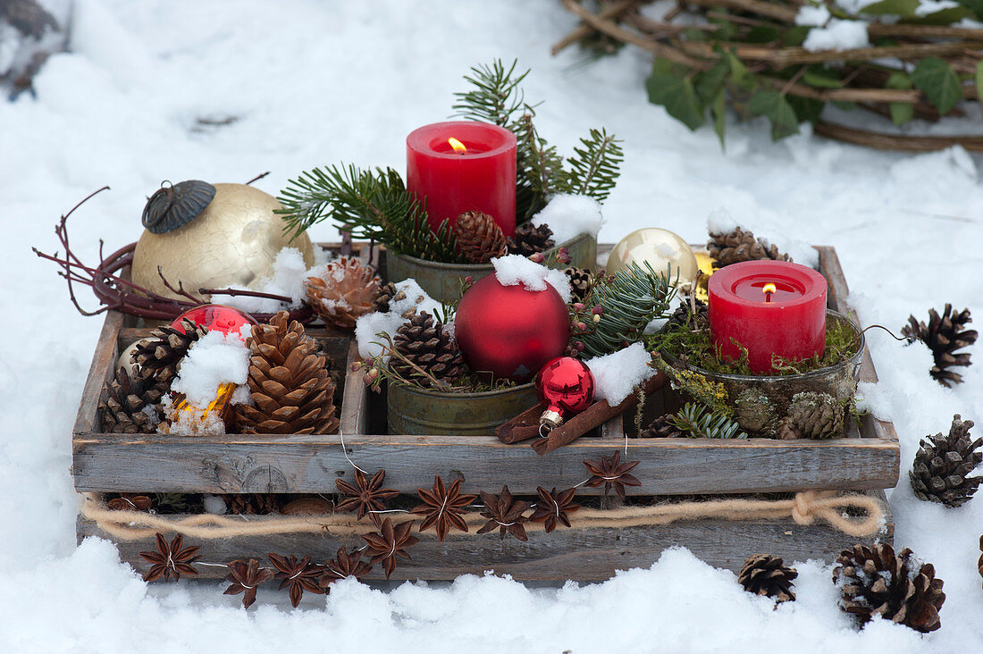 Wooden box with candles and Christmas tree decorations in the snow