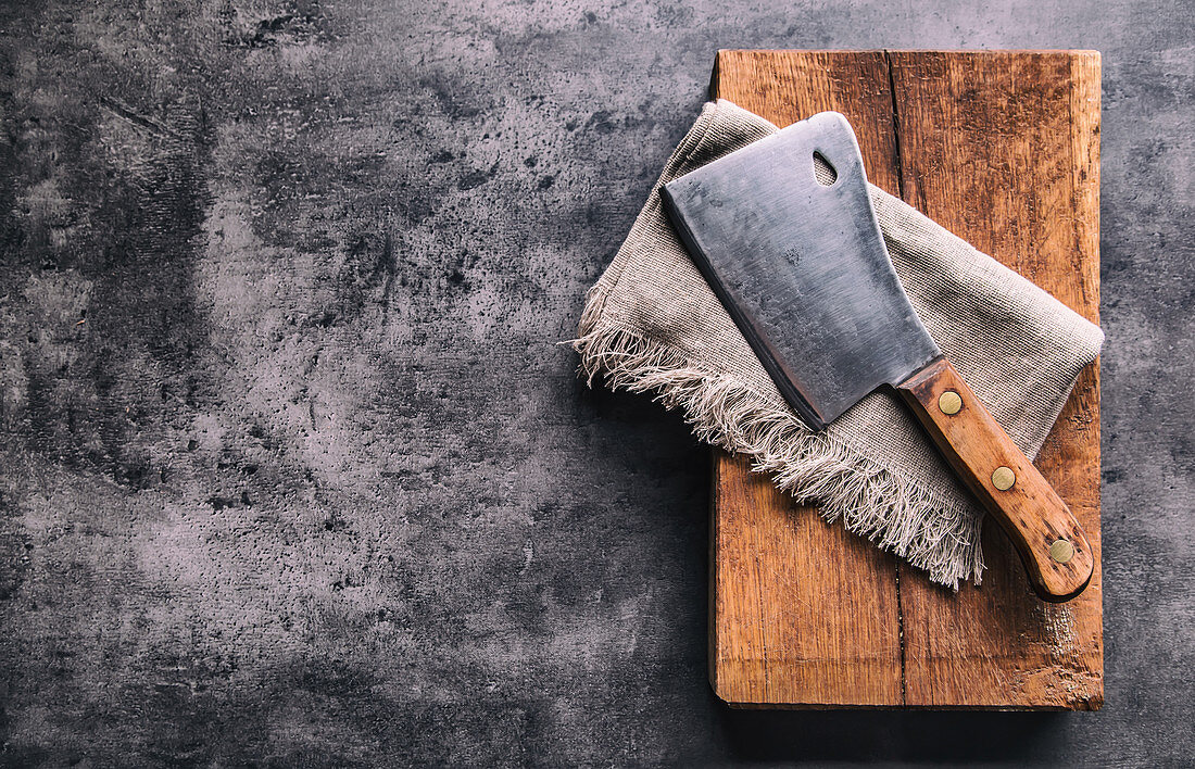 Vintage butcher meat cleavers with cloth towel on dark concrete or wooden kitchen board