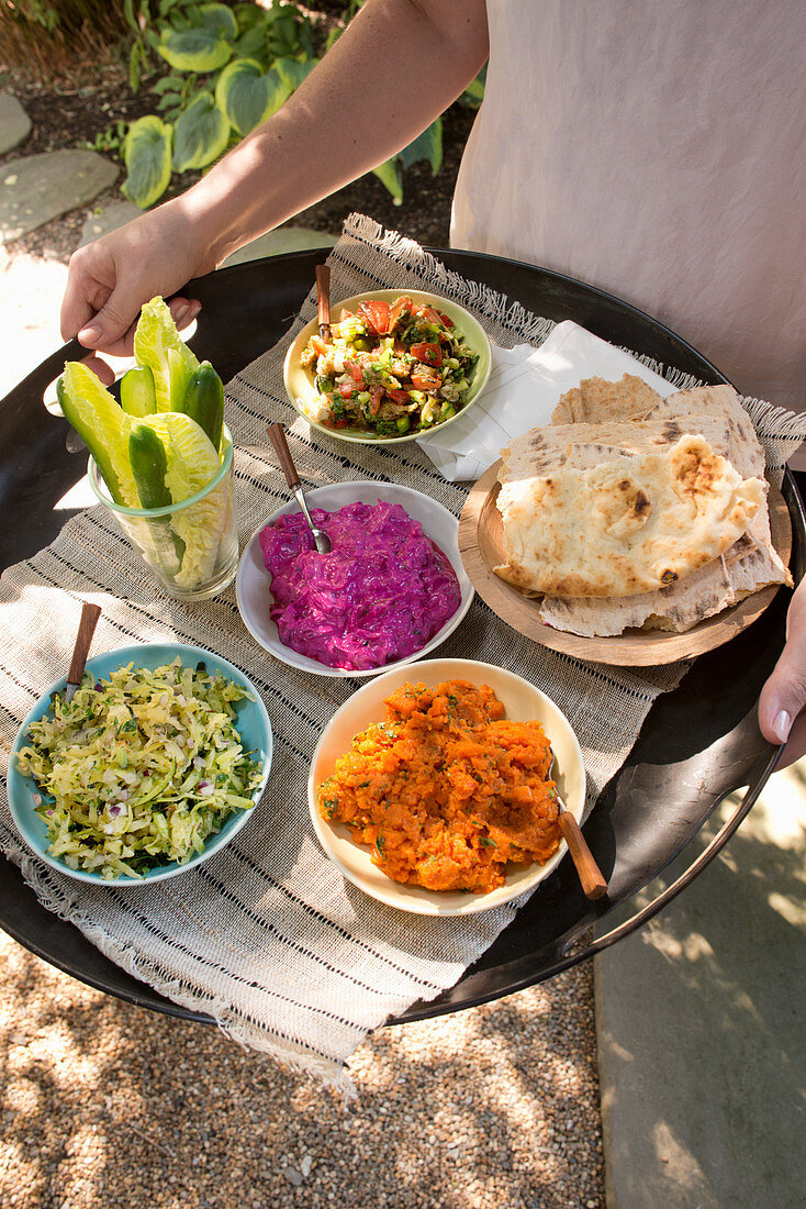 Frau serviert Salat, Dips und Fladenbrot auf Tablett im Garten