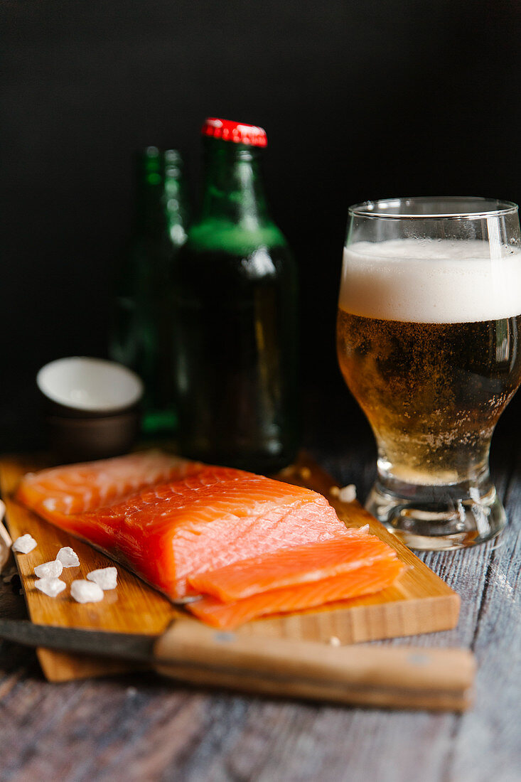 A fresh salmon fillet on a wooden board and a glass of beer