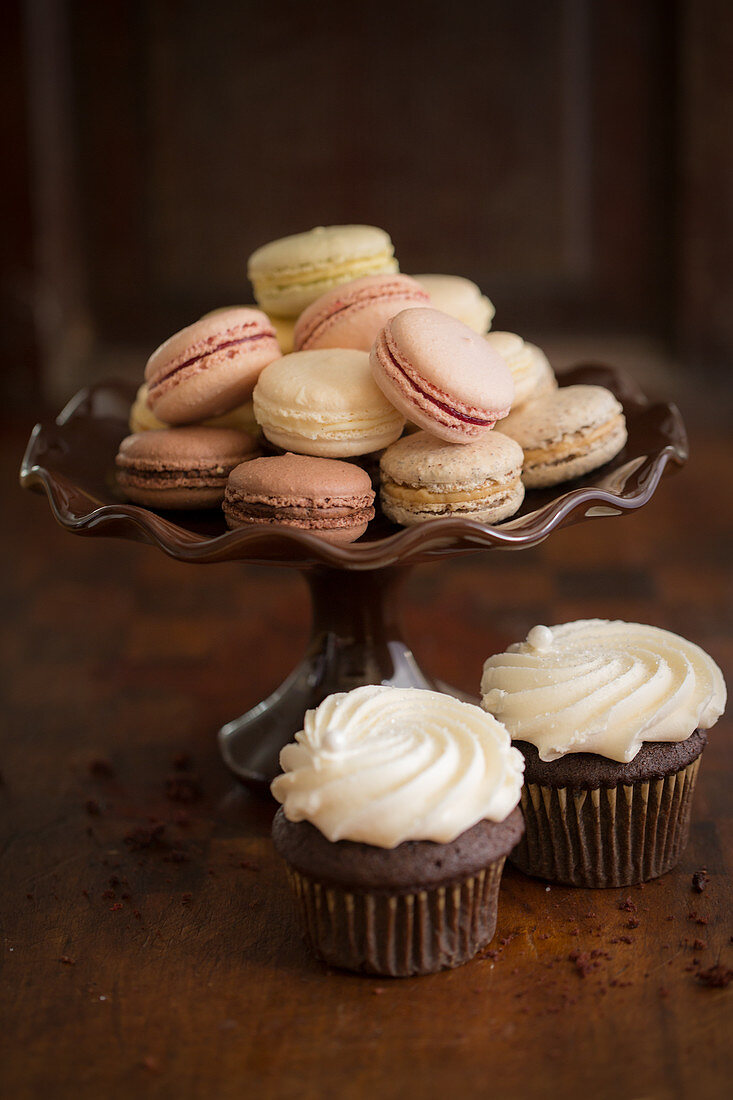 Macarons on a cake stand in front of two chocolate cupcakes
