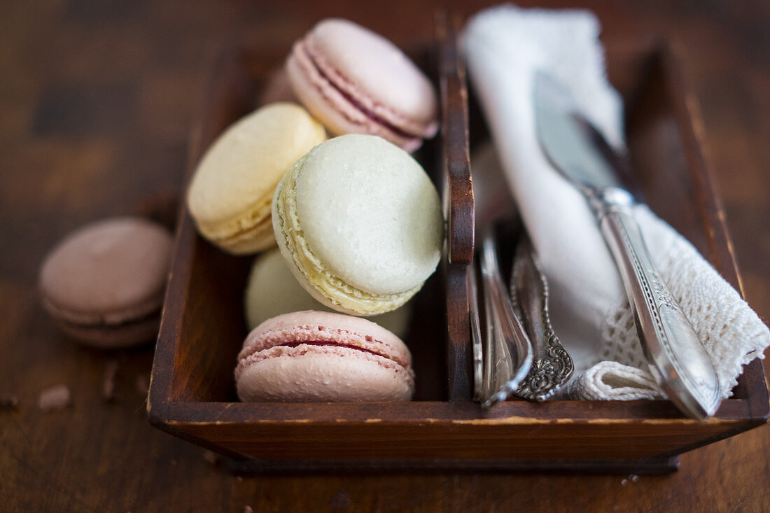 Various colourful macarons with cutlery and napkins in a wooden box