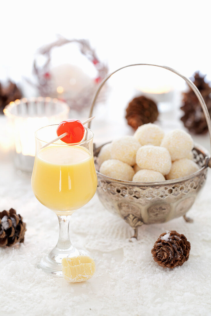 A glass of eggnog, and white egg liqueur chocolate truffles in a silver bowl